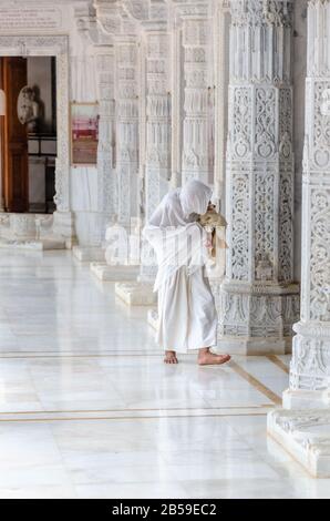 Eine sehr gealterte Frau, die ganz weiß gekleidet ist und bei einem der Jinalays im 72 Jinalaya Jain Temple, Mandvi, Kutch, Gujarat, Indien betet. Stockfoto