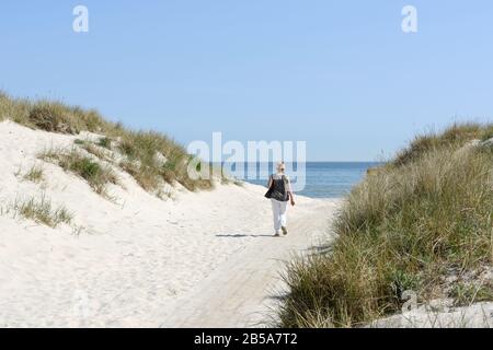 Eine Frau, die zu einem Strand mit Meer im Hintergrund läuft, Sandhammaren, Ystad, Skane, Schweden Stockfoto