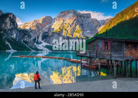 Backpacker Tourist mit Blick auf den See Braies. Malerischer Ort mit verschneiten Bergen und Holzbooten am See, in den Dolden, im Ital Stockfoto
