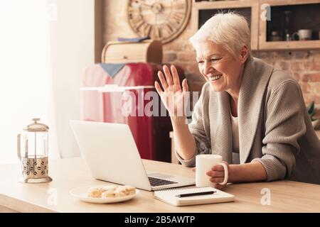 Ältere Frau, die in der Küche einen Videoanruf auf den Laptop macht Stockfoto