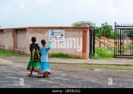 Zwei kleine Mädchen, die mit Schultasche laufen und das Schultor betreten, das vom Sarva Shiksha Abhiyan Logo in Gandhi Nu Gam, Kutch, Gujarat, Indien markiert ist Stockfoto