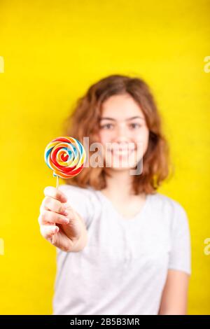 Teenager Mädchen hält mehrfarbigen runden Lollipop in ihrer Hand aus Stockfoto