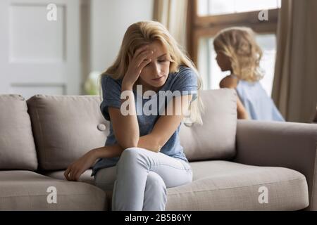 Müde Mama sitzt auf dem Sofa und hat Kopfschmerzen Stockfoto