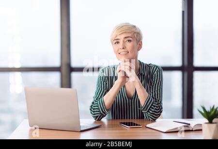 Selbstbewusste Geschäftsfrau, Die Lächelnd Im Modernen Büro Auf Dem Laptop Sitzt Stockfoto