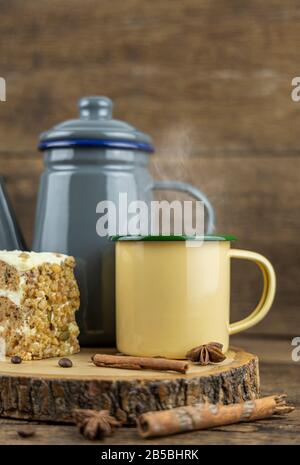 Eine gelbe Tinnetasse mit heißem Tee mit Teekanne und Kuchen auf Holztisch. Stockfoto