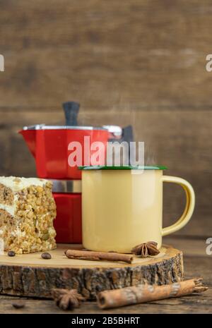 Eine gelbe Tasse heißen Kaffee mit italienischer Kaffeekanne (Moka) und Kuchen auf Holztisch. Stockfoto