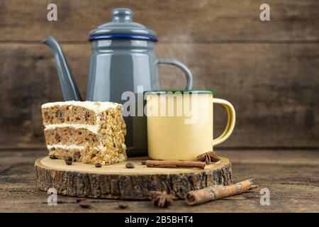 Eine gelbe Tinnetasse mit heißem Tee mit Teekanne und Kuchen auf Holztisch. Stockfoto