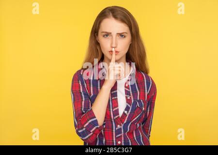 Shh, sei ruhig! Porträt des ernsthaften Ingwermädchens im karierten Hemd, das den Finger auf den Lippen hält, die Geste "Hush Silence" macht und darum bittet, geheim zu halten, spe nicht Stockfoto