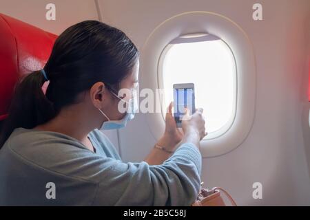 Asiatische Mädchen verwenden eine Schutzmaske für Coronavirus oder Kovid 19 im Flughafen. Asiatisches Mädchen fotografiert aus dem Fenster des Flugzeugs. Stockfoto