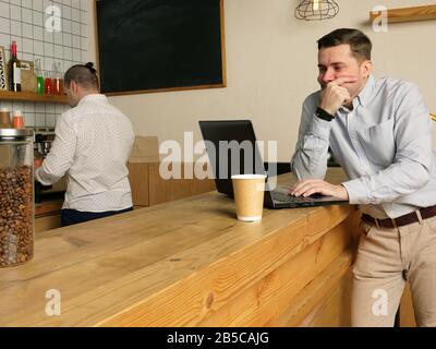 Penibler Mann liest aus Laptop im Café. Seriöser Mann arbeitet in der Cafeteria. Stockfoto