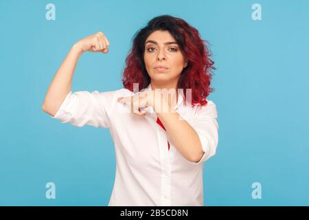 Schau, ich bin stark! Porträt der stolzen Frau mit ausgefallenen roten Haaren, die auf Bizeps auf der erhobenen Hand zeigt und die weibliche Kraft besitzt, Erfolg zu erzielen, Feminismus Co Stockfoto