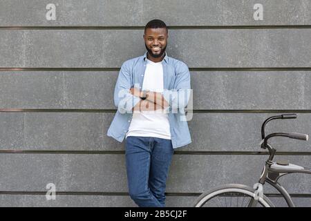 Fröhlicher Schwarzer Mann, Der An Der Wand Steht Und In Der Nähe Seines Fahrrads Steht Stockfoto