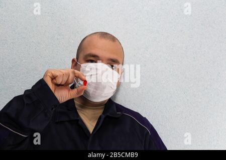 Ein Mann mittleren Alters in einer medizinischen Maske hält eine rote Pille. Schutz vor dem Virus. Stockfoto