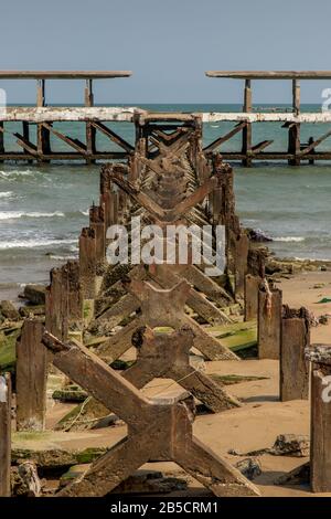 Blick auf Zerbrochene alte Struktur Überreste von Pier im Meer. Kleine Welle krachend in die texturierten rostigen Pierpfosten. Stockfoto