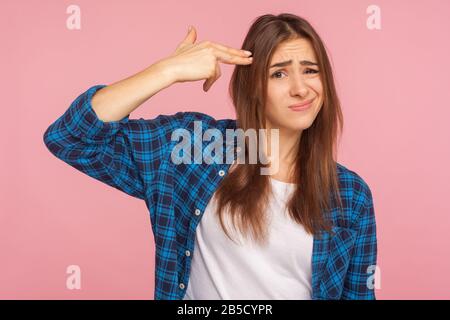 Bitte tötet mich! Porträt des depressiven Mädchens im karierten Hemd, das mit der Fingerpistole zum Kopf mit verzweifeltem Ausdruck strebte und sich mit Selbstmordgestik erschießt Stockfoto