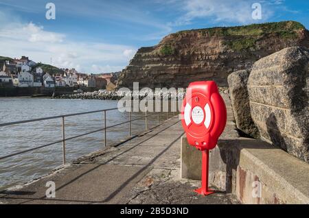 Ein Rettungsring für Wassernotfälle im hübschen Küstenhafen von Staithes, einem malerischen Dorf an der Küste von North Yorkshire, Großbritannien Stockfoto