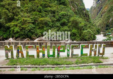 Machu Picchu Pueblo, Peru - 8. Januar 2019: Schild mit dem Namen der Stadt am Straßenrand von Machupicchu Pueblo oder Aguas Calientes mit dem Fluss Urubamba in Back, Peru Stockfoto