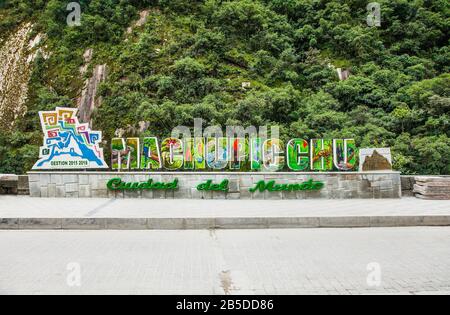 Machu Picchu Pueblo, Peru - 8. Januar 2019: Schild mit dem Namen der Stadt am Straßenrand von Machupicchu Pueblo oder Aguas Calientes mit dem Fluss Urubamba in Back, Peru Stockfoto