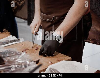 Männerhände schneiden Wurst auf einem Holzschneidebrett. Stockfoto