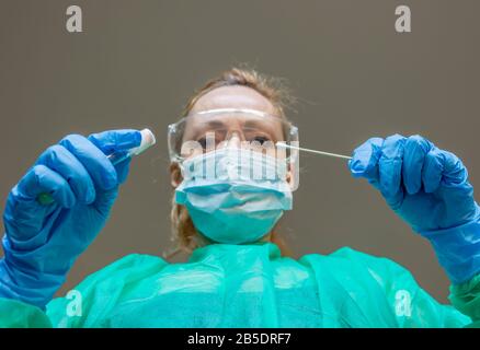 Eine blonde weiße Frau, die als Labortechnikerin arbeitet, führt einen Tupfer durch, um auf eine mögliche Coronavirus Covid-19-Infektion zu prüfen Stockfoto