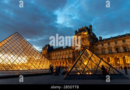 Abendansicht des Louvre Museums mit den Pyramiden beleuchtet und einem dramatischen Himmel in Paris, Frankreich. Stockfoto