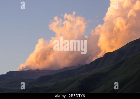 Cumulus-Wolken färbten durch die untergehende Sonne über den Drakensberg in Südafrika eine goldene pinkische Farbe Stockfoto