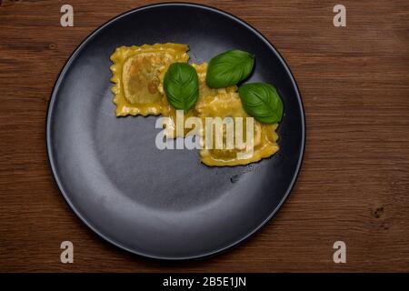 Frische, unbehackte handgefertigte italienische Tortellini- und Ravioli-Pasta mit Basilikum auf einer dunkel strukturierten Platte mit von oben betrachtet Platz für Kopien Stockfoto