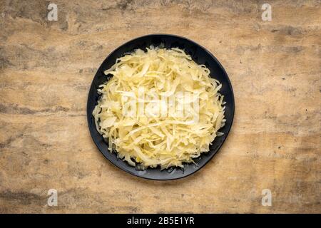 Schwarze Platte mit Sauerkraut vor strukturiertem Papierhintergrund, präbiotisches Konzept - fermentierte Lebensmittel gut für die Darmgesundheit Stockfoto