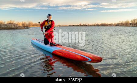 Senioren-Paddler in einem Trockenanzug und einer Schwimmweste paddeln auf einem See in Colorado, im Winter oder im Frühjahr auf einem langen Rennstativ auf. Stockfoto