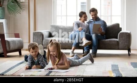 Kleine Kinder zeichnen Bilder, während Eltern ein digitales Tablet verwenden. Stockfoto