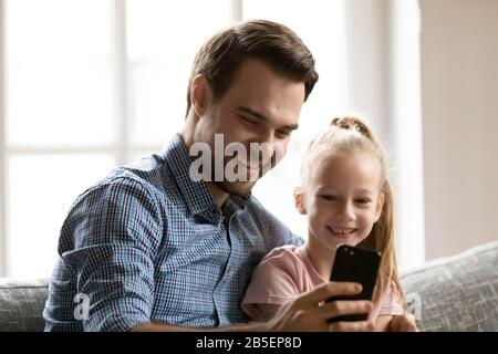 Lächelnder Vater nimmt selfie mit Tochter auf dem Handy auf. Stockfoto