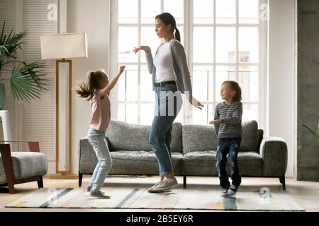 Fröhliche junge Mutter tanzt mit kleinen Kindergeschwistern. Stockfoto