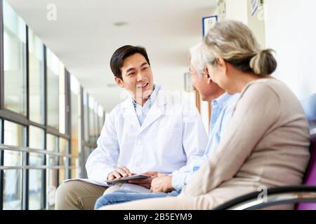 Freundlicher junger asiatischer Arzt, der mit dem alten Paar im Flur des Krankenhauses spricht Stockfoto