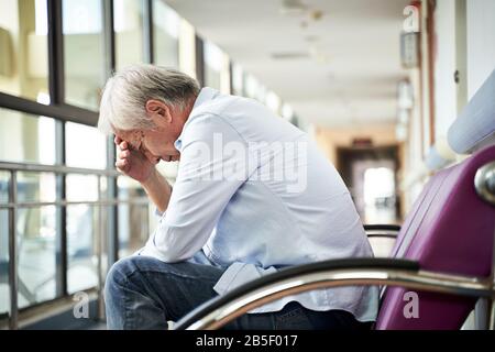 Asiatischer alter Mann, der auf dem Flur des Krankenhauses sitzt, sieht traurig und depressiv aus Stockfoto