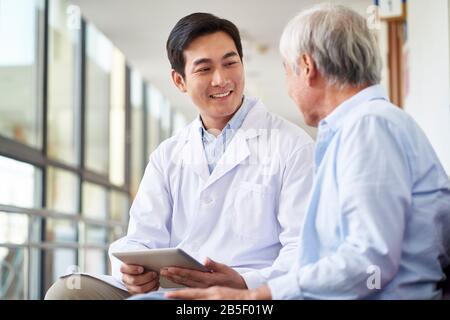 Freundlich lächelnder junger asiatischer Arzt, der das Testergebnis für ältere Patienten im Krankenhaus spricht und erklärt Stockfoto