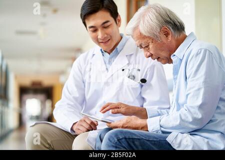 Freundlich lächelnder junger asiatischer Arzt, der das Testergebnis für ältere Patienten im Krankenhaus spricht und erklärt Stockfoto