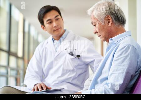 Junger asiatischer Arzt spricht und erklärt das Testergebnis und die Diagnose demoralisierten älteren Patienten im Krankenhausflur Stockfoto