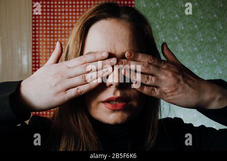 Erschrockene Frau betucht ihre Augen mit Händen, die Angst haben und missbraucht werden, sich zu verstecken Stockfoto