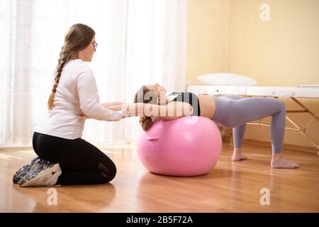 Physiotherapeuten arbeiten mit jungen weiblichen Client auf die Kernkompetenz mit fitball. Rehabilitation und Physiotherapie Hintergrund. Stockfoto
