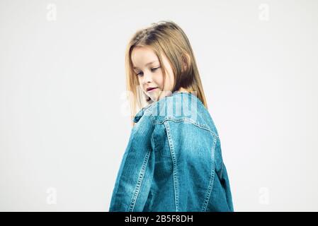 Aufdringliches Kinderporträt. Kleines Mädchen in Denimjacke posiert im Studio. Kindermode. Grauer Hintergrund. Porträt Stockfoto