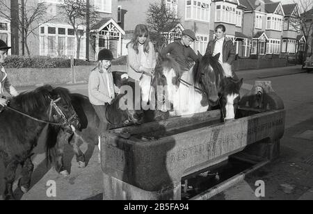 In den 1970er Jahren, historisch, halten Jugendliche auf Pferden und Ponys in einer ehemaligen Wasserrinne aus Stein, die im Jahre 1888 errichtet wurde, um ihren Tieren während eines heißen Sommers Erfrischung zu geben, South London, England. Im Laufe des Jahrzehnts waren einige der Sommer extrem heiß. Stockfoto