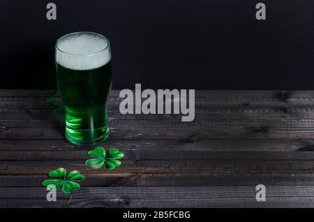 Urlaub St. Patrick's Day. Grünes Bier mit Kleeblatt auf dunklem Holzhintergrund mit Kopierraum. März 17. Stockfoto