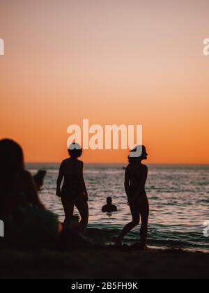 Einige Silhouetten von Menschen am Ufer von A versammelt Strand bei Sonnenuntergang in Australien Stockfoto