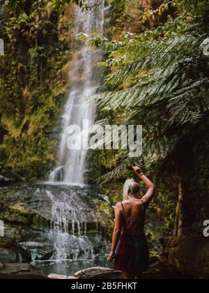 Eine junge Frau, die durch Australien reist und einen faszinierenden Wasserfall in einem Regenwald erkundet. Stockfoto