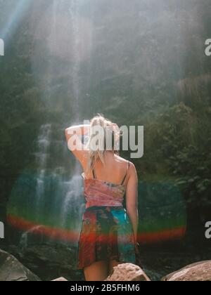 Eine junge Frau, die durch Australien reist und einen faszinierenden Wasserfall in einem Regenwald erkundet. Stockfoto