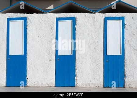Drei kleine pastellblaue und weiße Vintage-Türen aus Holz an einer weiß gestrichenen Wand Stockfoto
