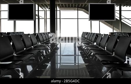 Reihen schwarzer Stühle am Flughafen mit leeren Bildschirmen und weißen Fenstern, Es gibt einen Weg für alle Fenster Stockfoto