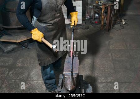 Weibliche Hände schmiegen in einer traditionellen Schmiede ein warmes Metall-Werkstück auf dem Amboss Stockfoto