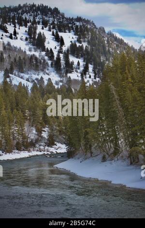 Der eisige Fluss schlängelt sich durch eine schneebedeckte Landschaft in den Bergen. Stockfoto