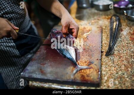 Küchenchef schneidet frischen Fisch auf dem Fischmarkt mit einem scharfen Messer auf einem Schneidebrett von Hand. Sushi, Abendessen, Mittagessen. Japanische Küche und asiatische Küche Stockfoto